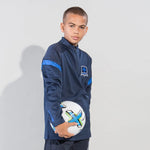 Boy wearing a navy kinetic sports jacket with a logo, holding a football