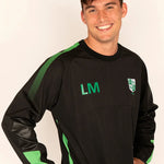 A smiling man wearing a black long-sleeve athletic top with green accents, including green mesh panels on the shoulders, green 'LM' initials on the chest, and a green and white shield crest on the left chest